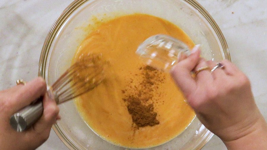 Overhead shot of whisk together eggs, butter, half and half, pumpkin, milk, sugar, salt, and pumpkin pie spice in a mixing bowl.