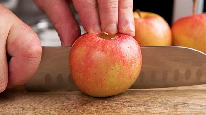 Side shot of a cored apple being sliced in half.