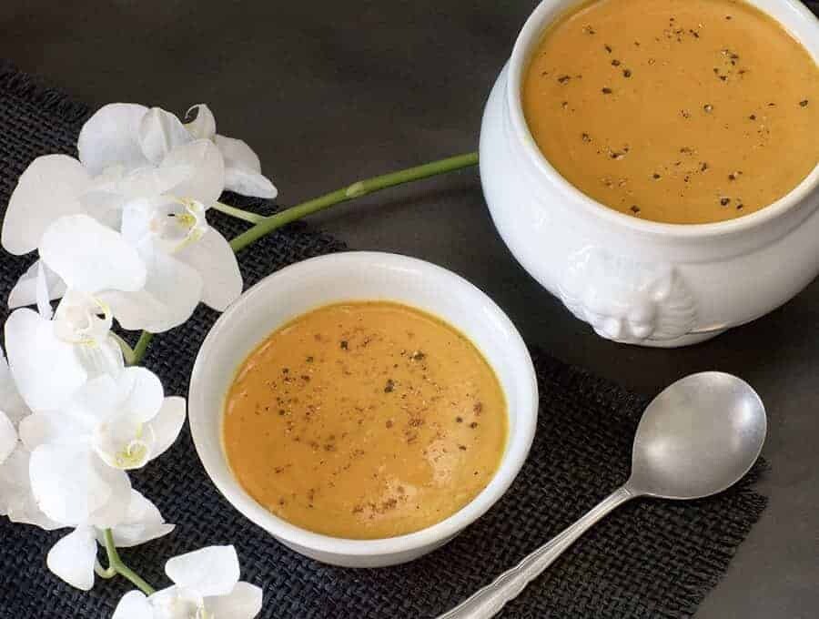 Two bowls of Butternut Ginger Soup with flowers and a spoon.