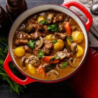 Beef meat stewed with potatoes, carrots and spices in cast iron pan on burned black wooden background