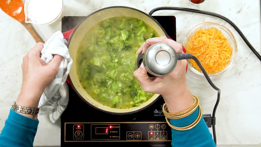 Overhead shot of using an immersion blender to blend some of the broccoli in the pot.