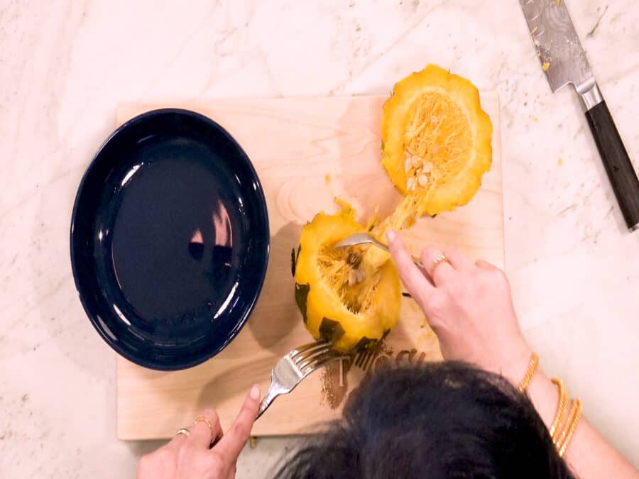 Overhead shot of using a fork and grapefruit spoon to remove the seeds from the squash.