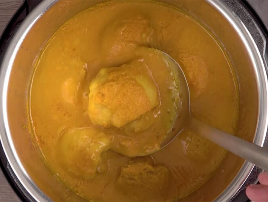 cooked chicken chunks on a large spoon in a yellow sauce