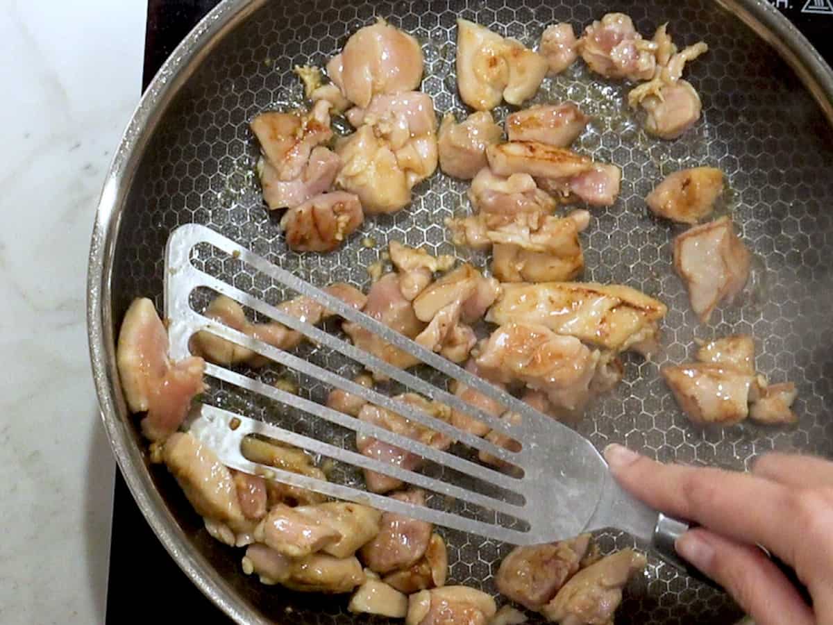 hald cooked diced chicken in a skillet with a metal spatula