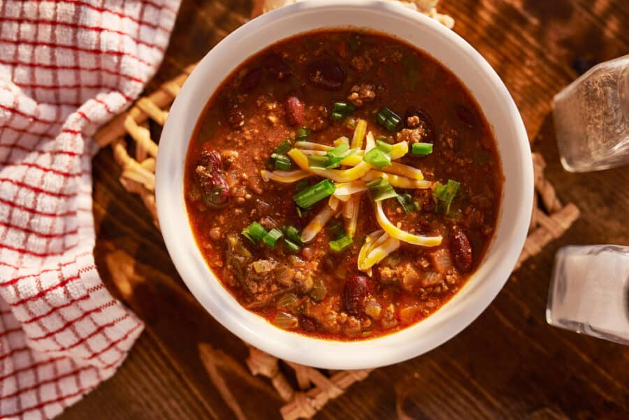 overhead photo of a bowl of chili with cheese and green onions