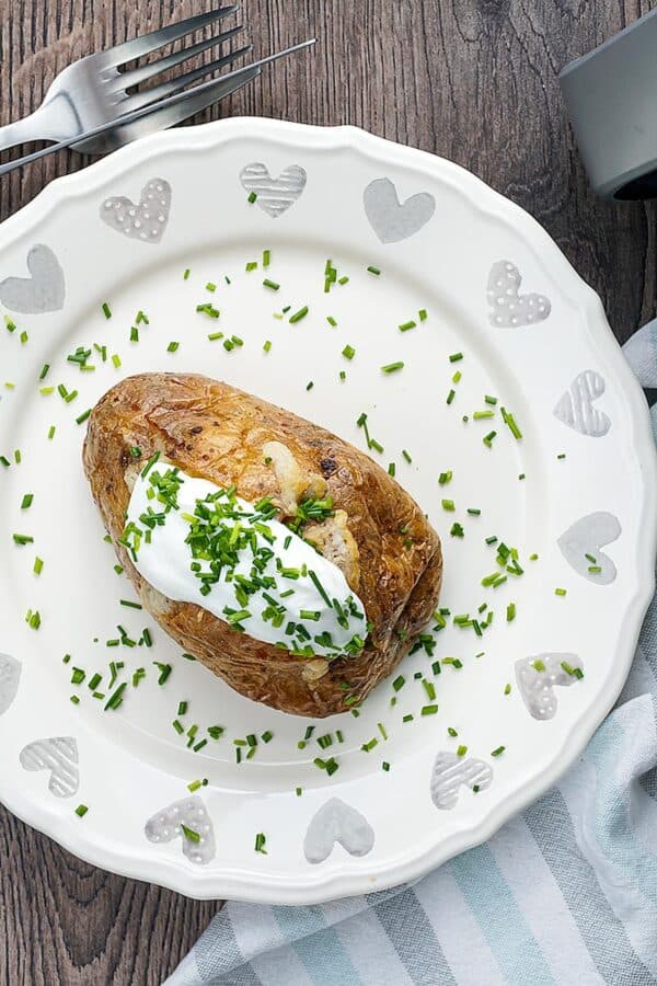 Overhead shot of an air fryer baked potato on a white plate