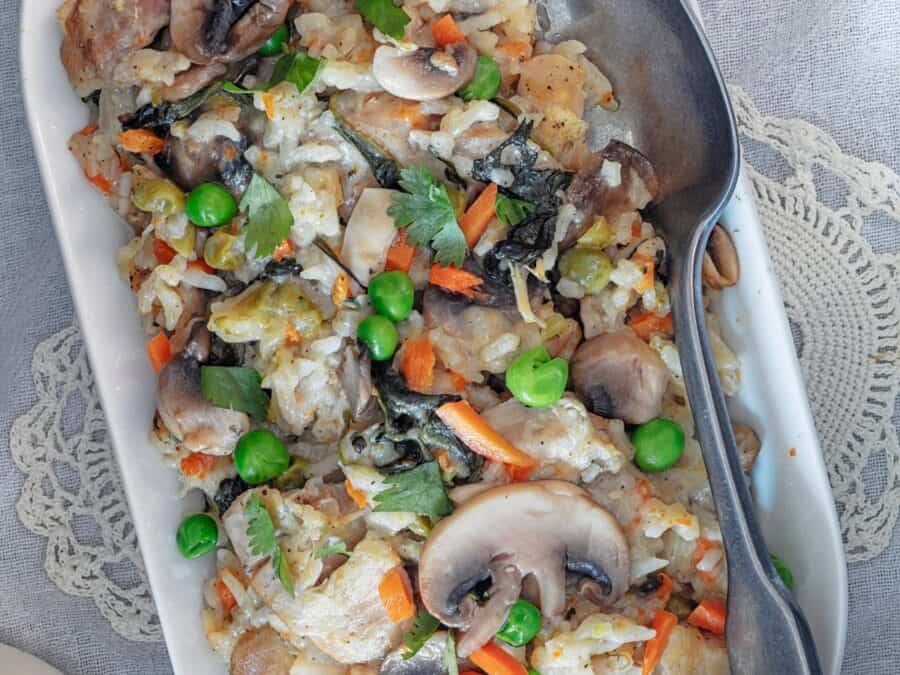 Creamy Chicken and Rice with mushrooms, peas, and carrots served on a white platter. A spoon is placed to the side for serving.