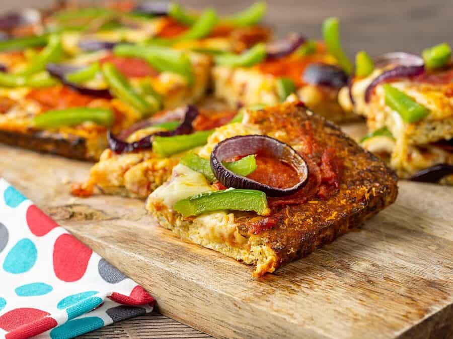 slices of low carb pizza on a cutting board. the pizza slices are topped with onions, peppers, cheese, and sausage.