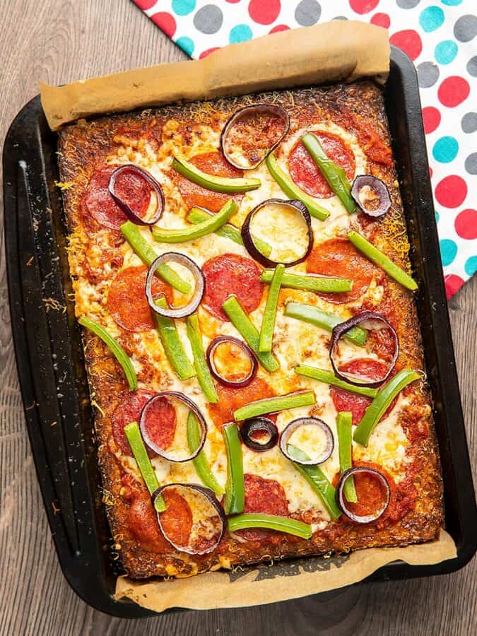 Overhead shot of keto pizza topped with tomato sauce, red onions, bell peppers, salami, and cheese