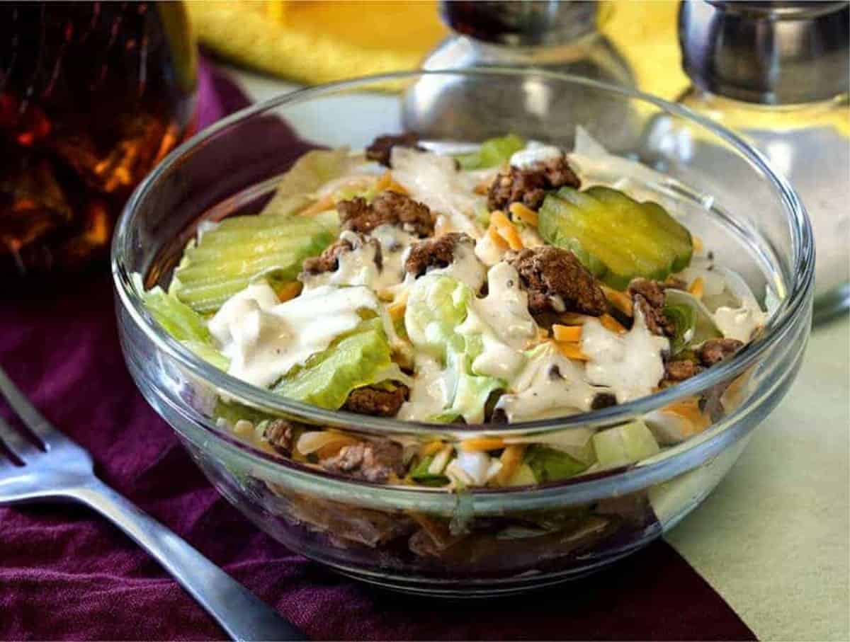 Big mac salad served in a clear glass bowl over an indigo table cloth. 