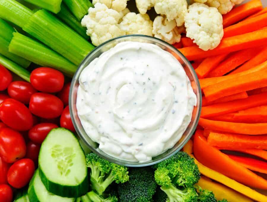 An over head image of a  vibrant vegetable tray with a glass bowl of dip in the center. 