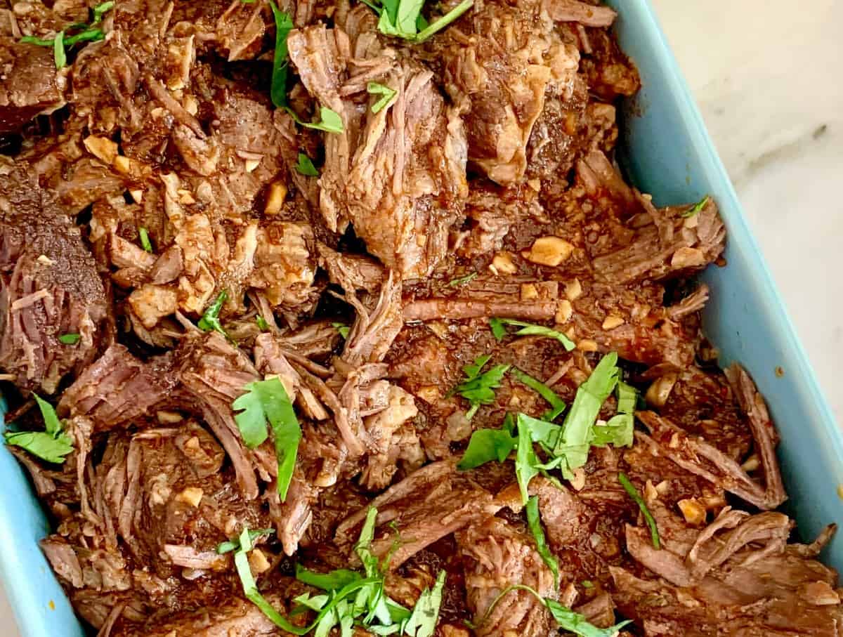 Lightly sauced shredded beef barbacoa served in a light blue serving dish. 