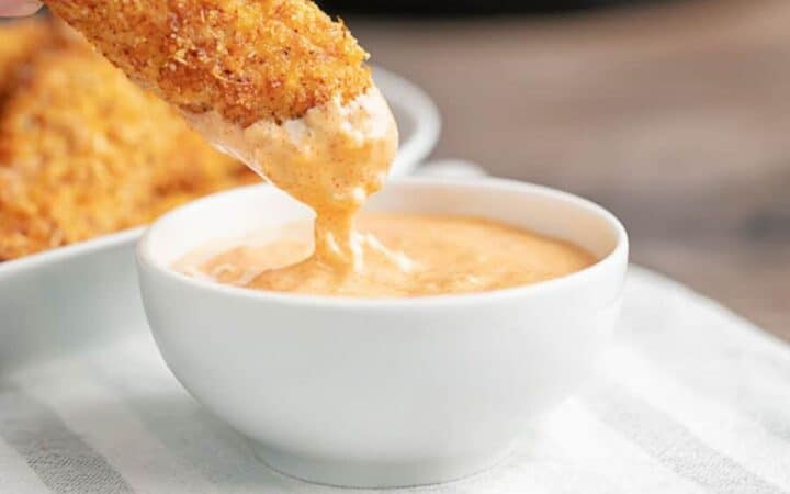 A Keto Chicken Tender being dipped in a white bowl of Big Mac Sauce