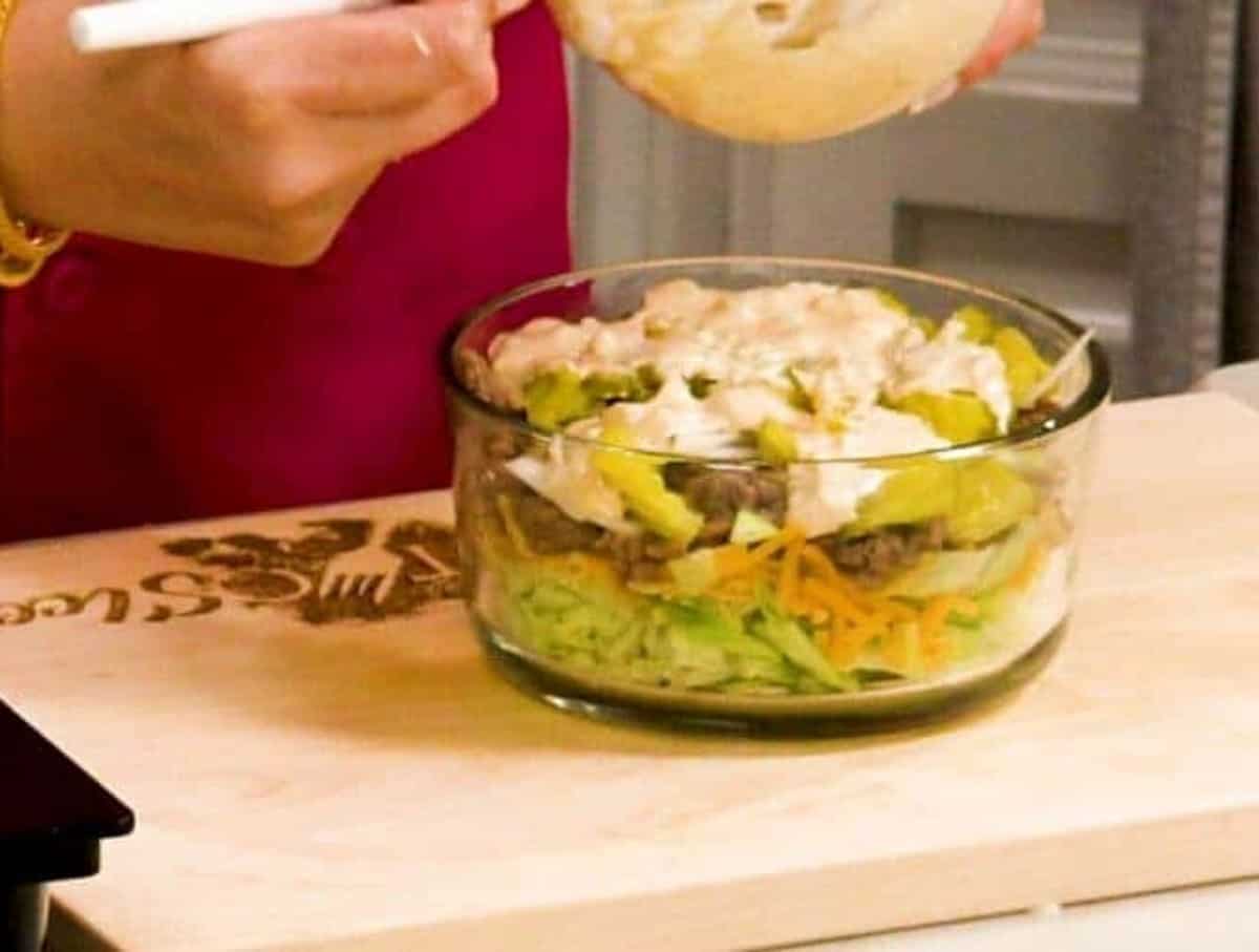 Big Mac Salad in a glass bowl on a wooden cutting board