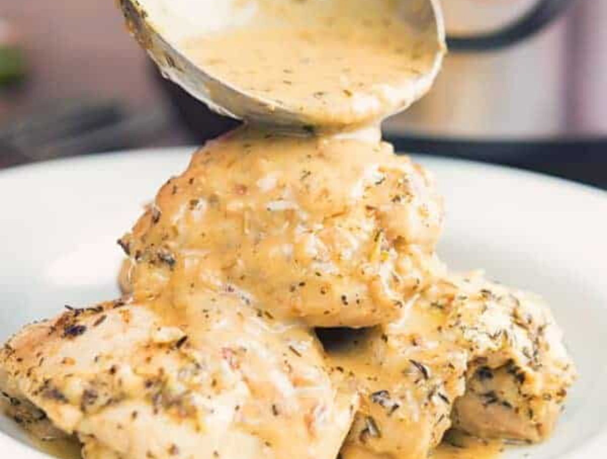 Creamy Garlic Chicken Served in a white bowl with a ladle pouring sauce over the top.
