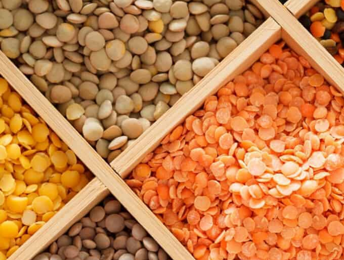 Close up image of a rainbow of lentils inside of a wooden container dividing them by color.