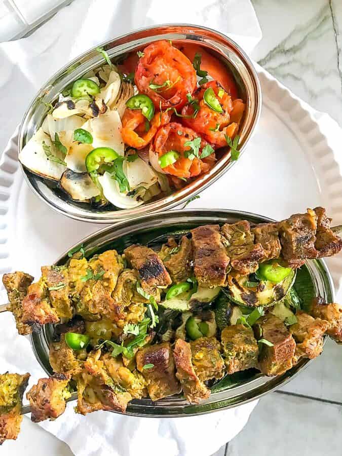 kebabs and grilled vegetables in silver platters on a white plate