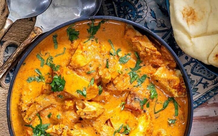 Butter Chicken Served in a navy bowl with a side of naan