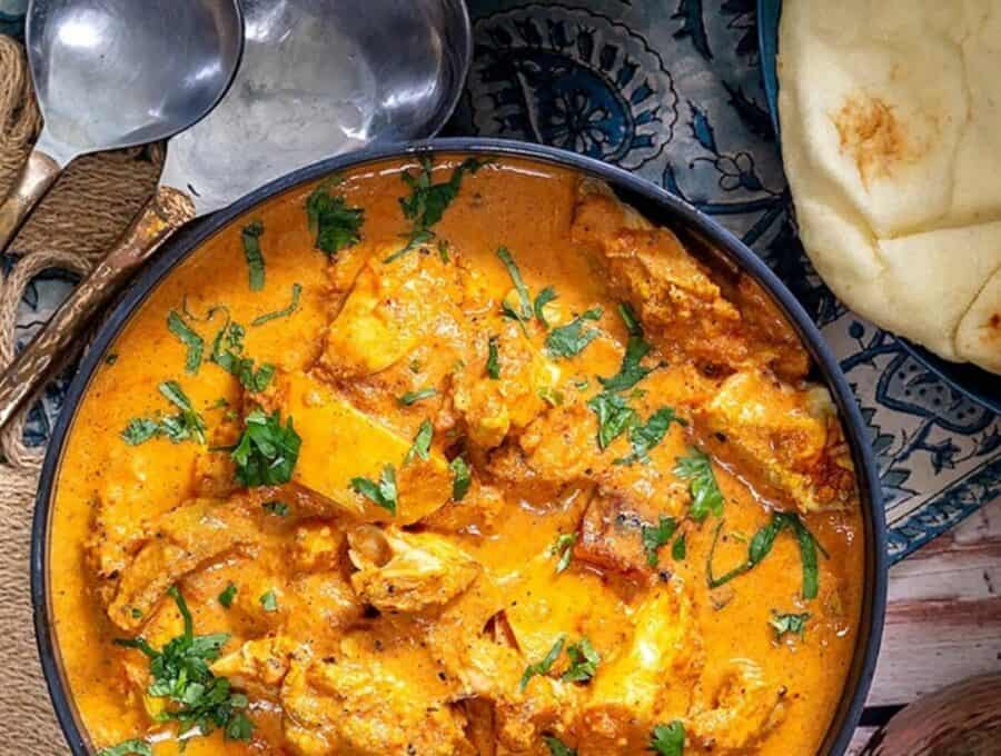 Butter Chicken Served in a navy bowl with a side of naan