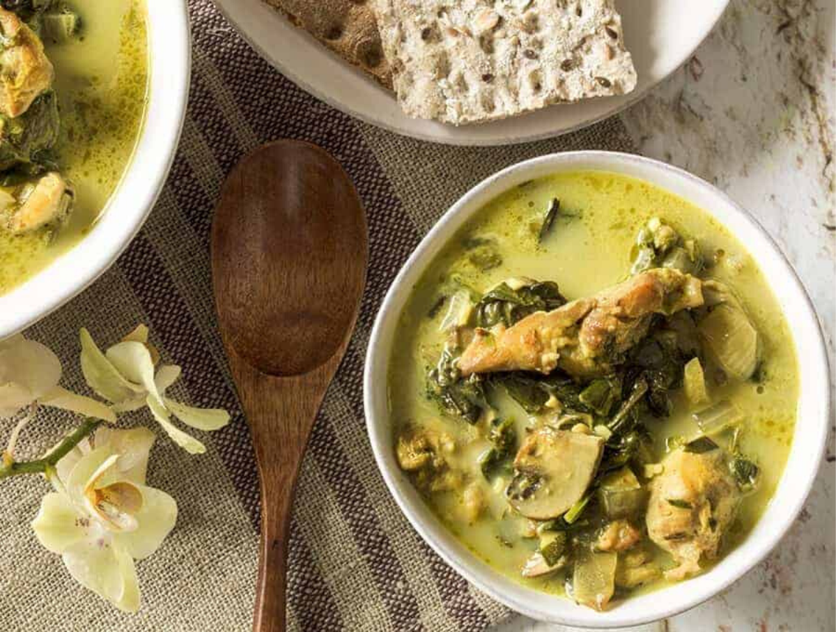 Overhead image of Chicken Curry Soup in a white bowl with a wooden spoon laying next to it on a table.