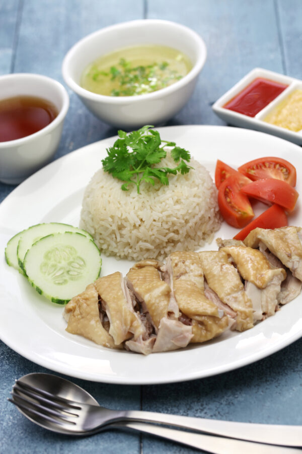 Hainanese Chicken and Rice served on a white plate with omatoes and cucumber.