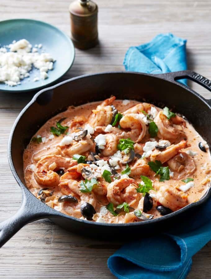 Instant Pot Shrimp Saganaki served in a cast iron pan with a bowl of feta cheese in the background.