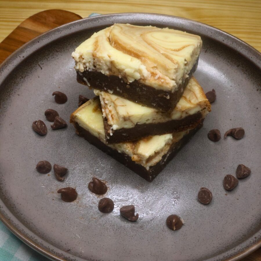 Three Keto Cheesecake Brownies stacked on top of eachother with sugar free chocolate chips surrounding them