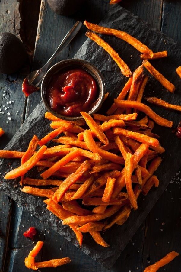 air fryer sweet potato fries on a dark cutting board with a side of ketchup