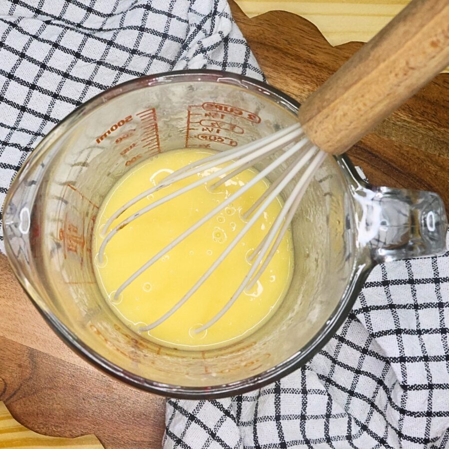 Egg, vanilla, and melted butter in a glass measuring cup with a whisk