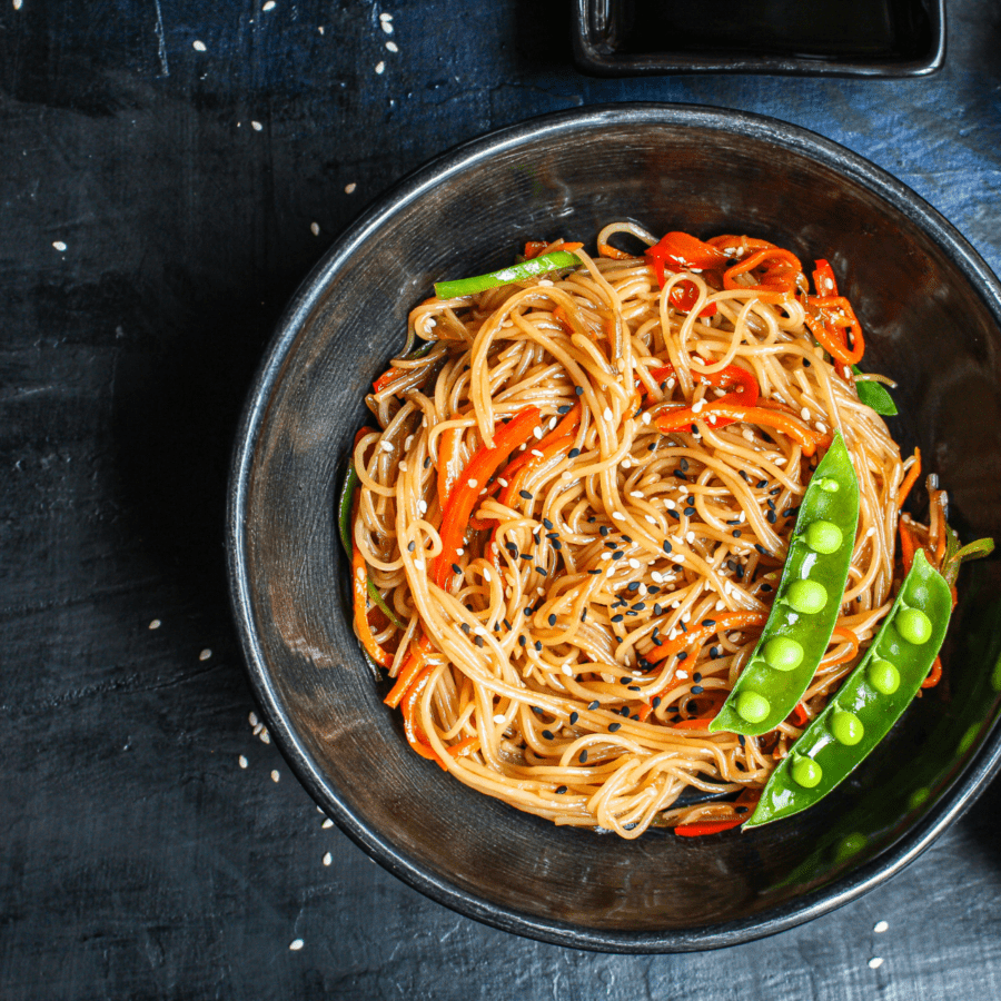 Spicy noodles in a dark colored bowl against a black backdrop
