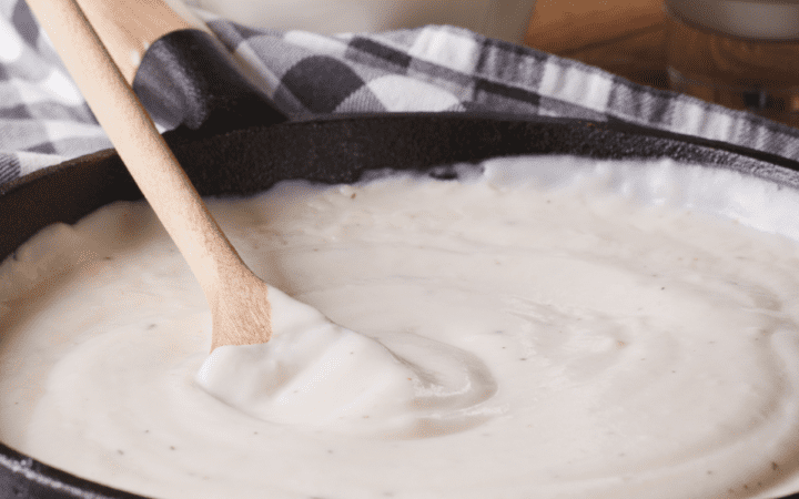 Keto Alfredo Sauce being stirred in a pan by a wooden spoon