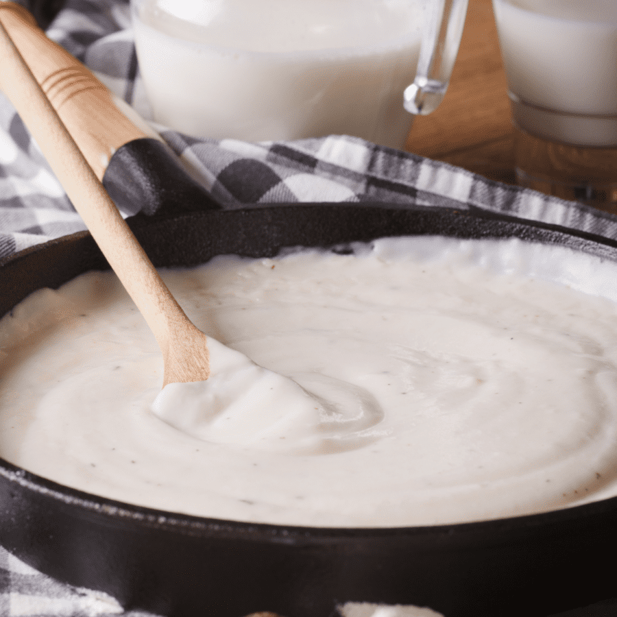 Keto Alfredo Sauce being stirred in a pan by a wooden spoon