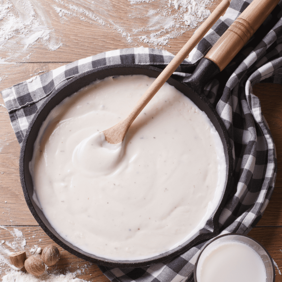 Overhead image of Keto Alfredo Sauce in a pan with a wooden spoon inside of the pan