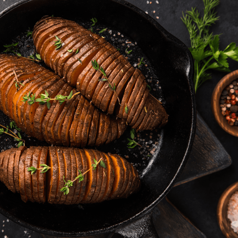 Overhead view of hasselback sweet potatoes in a skillet with spices and garnish on the side