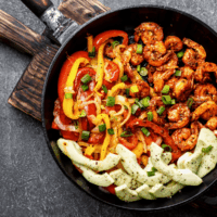 Shrimp Fajitas in a skillet on top of a wooden board