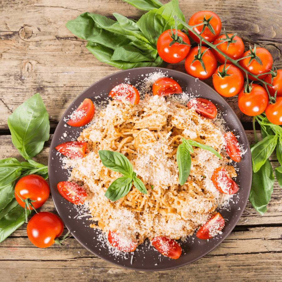 Chicken Spaghetti with Rotel on a wooden table surrounded by tomatoes on the vine