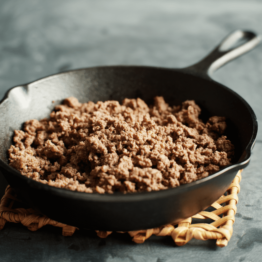 Close up of ground beef cooked in a cast iron skillet on a wooden trivet
