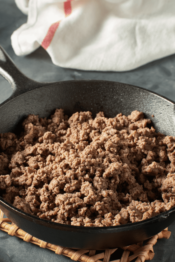 Ground beef cooked in a skillet sitting on a wooden trivet