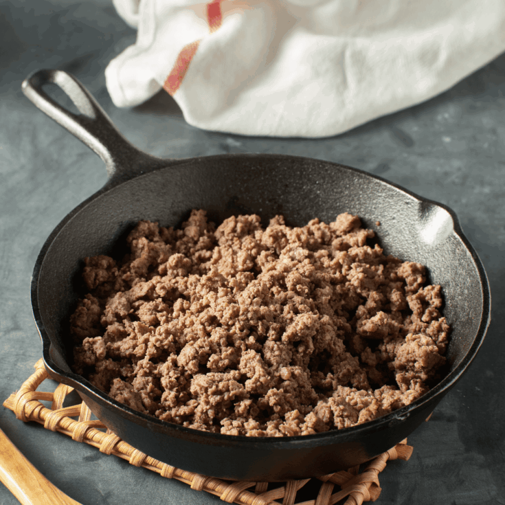 Ground beef cooked in a skillet sitting on a wooden trivet