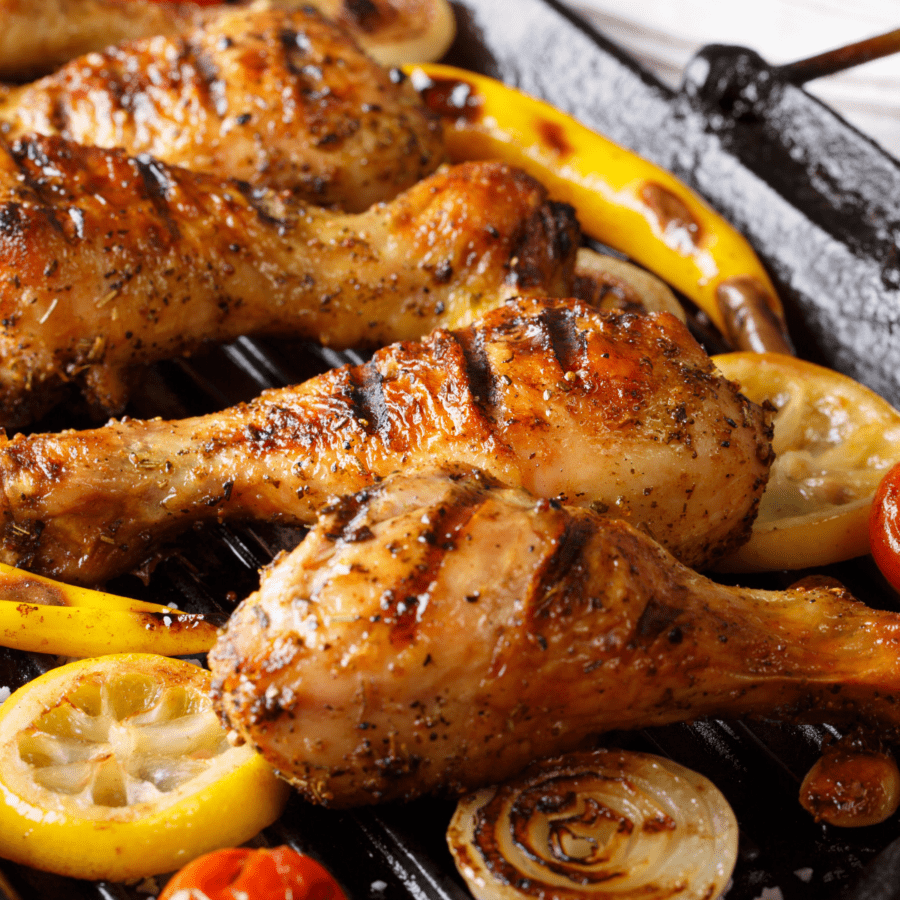 Close up of lemon pepper chicken next to grilled fruits and veggies