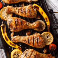 Lemon Pepper Chicken Drumsticks arranged next to grilled lemons and peppers