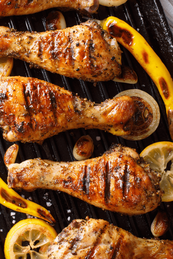 Lemon Pepper Chicken Drumsticks arranged next to grilled lemons and peppers