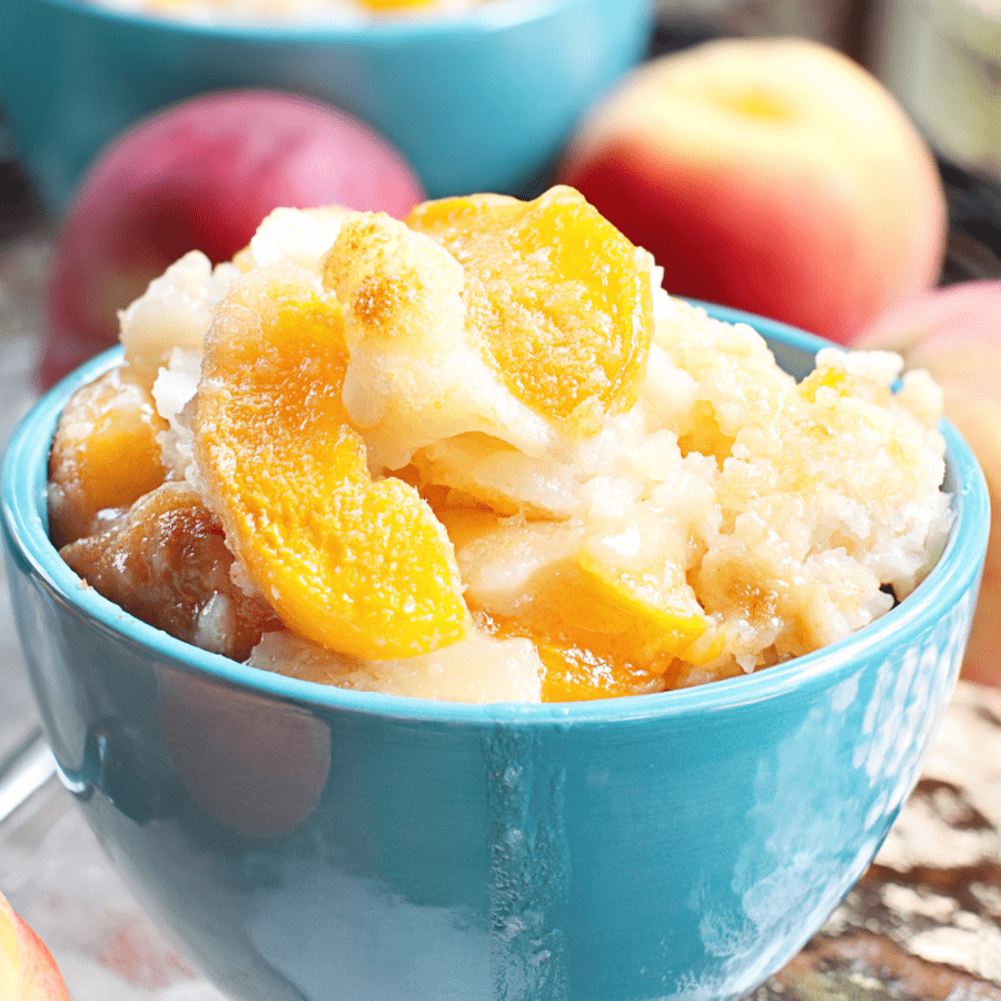 Peach Cobbler Dump Cake in a blue bowl with peaches in the background