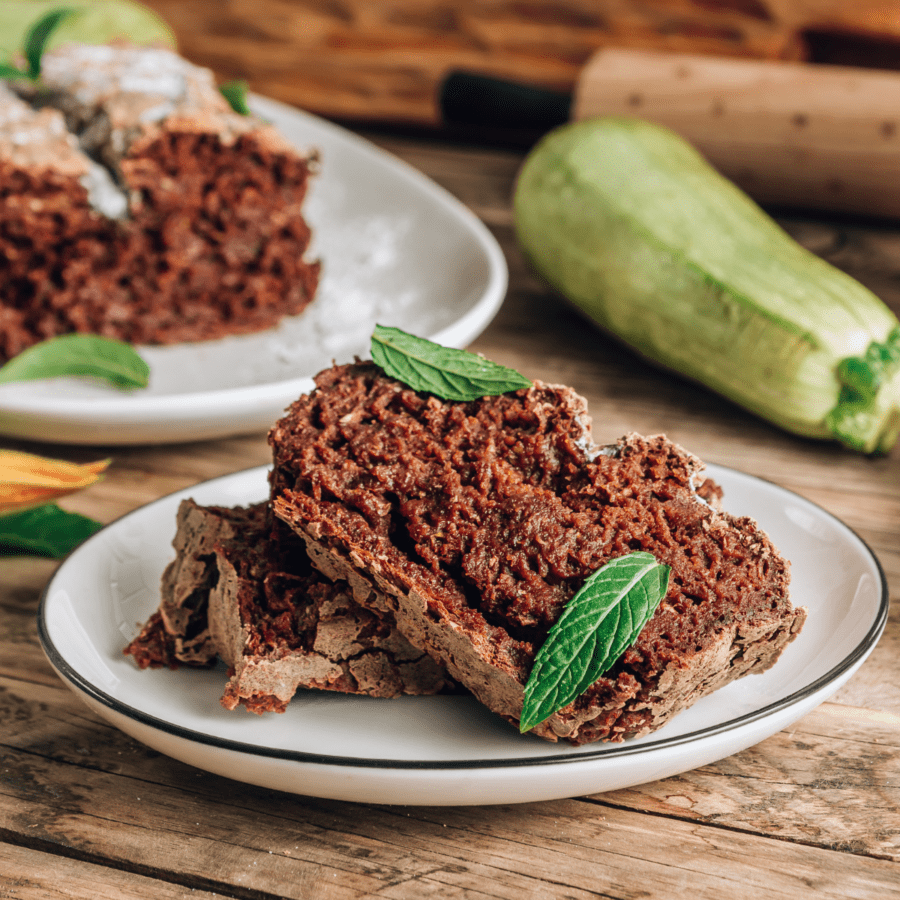 Two slices of zucchini cake on a white plate with the rest of the cake in the background