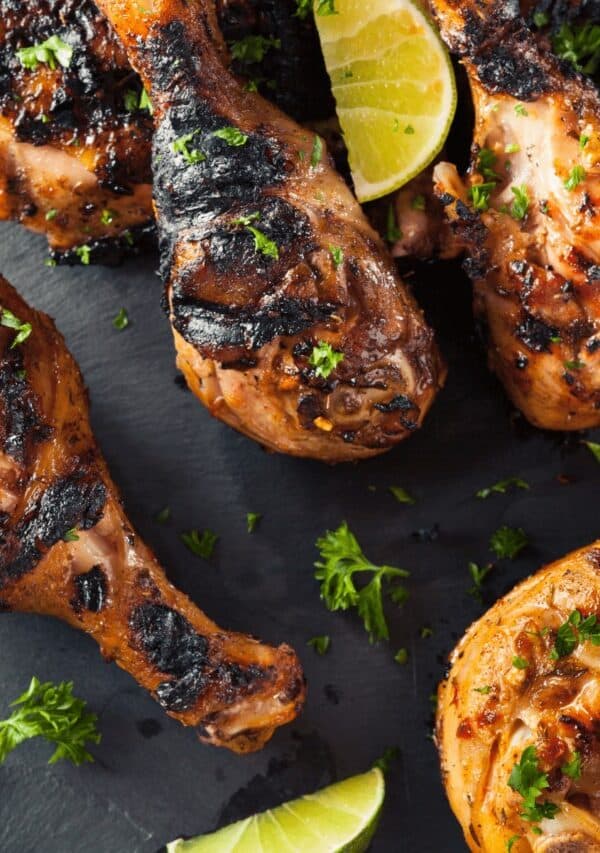 Blackened Chicken Drumsticks on a black background with cilantro and lime garnish