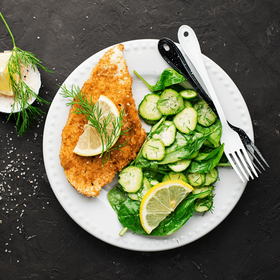 Overhead image of chicken milanese on a white plate with a green salad
