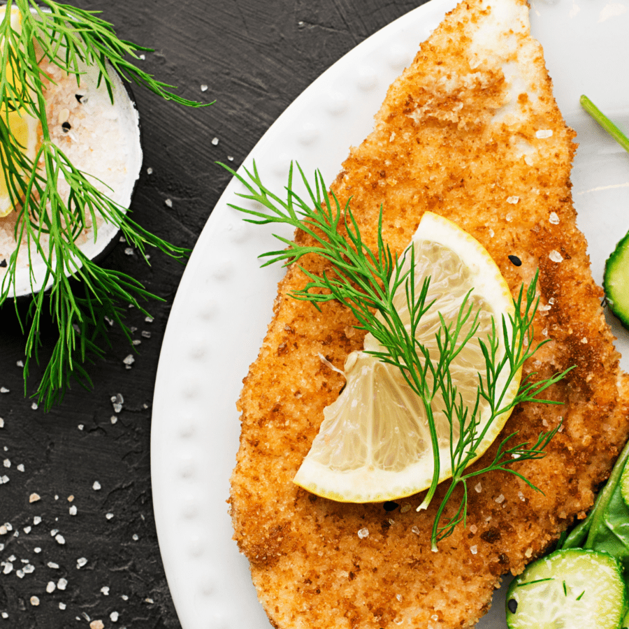 Close up image of chicken milanese on a white plate with a dill and lime garnish