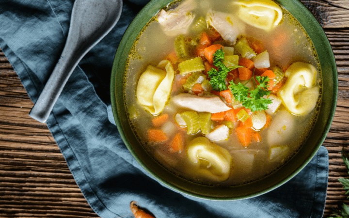 Overhead shot of chicken tortellini soup in a bowl witha blue napkin laying around it