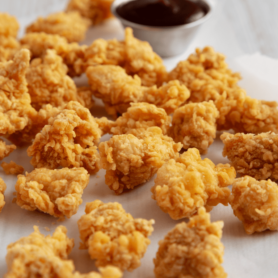 Popcorn chicken on a white surface with a dipping sauce
