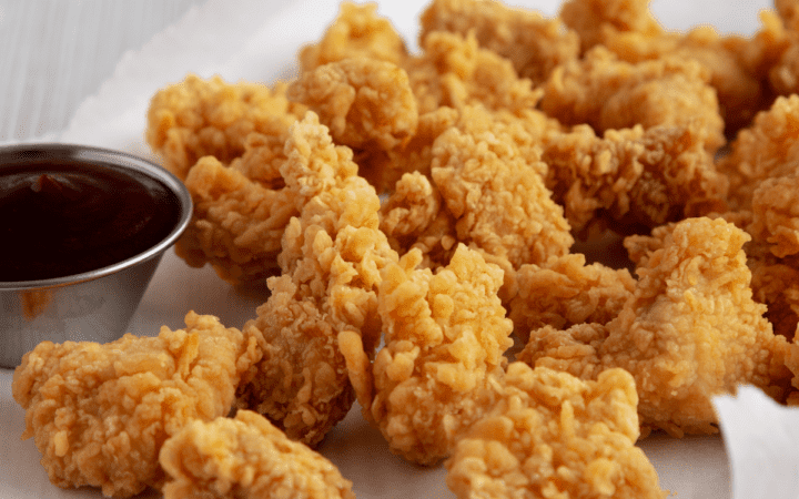 Popcorn chicken on a white surface with a dipping sauce on the side